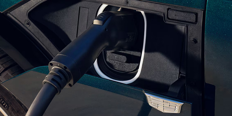 Close-up of a black electric vehicle charging cable plugged into the charging port of a dark green Cadillac vehicle.