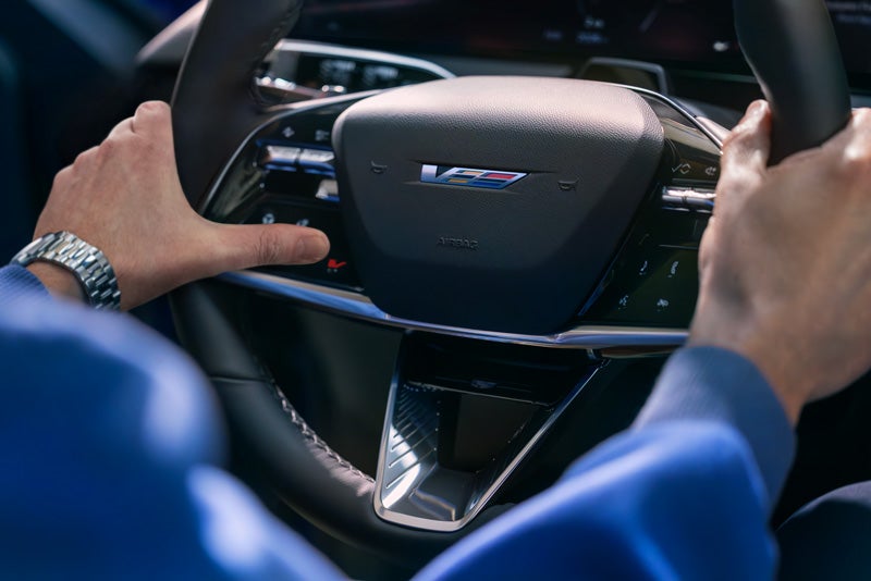 Close-up of a Man About to Press the V-Button on the 2026 OPTIQ-V Steering Wheel | Hudson Cadillac in Poughkeepsie NY