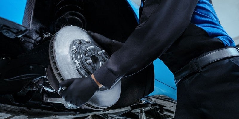 A technician wearing black gloves installing a disc brake rotor on a vehicle.