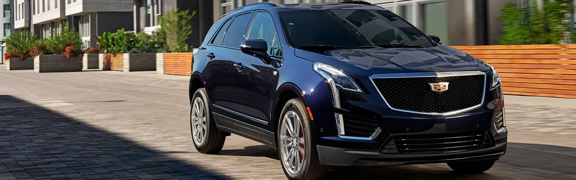 Pre-owned dark blue Cadillac XT5 SUV driving down a paved urban street.