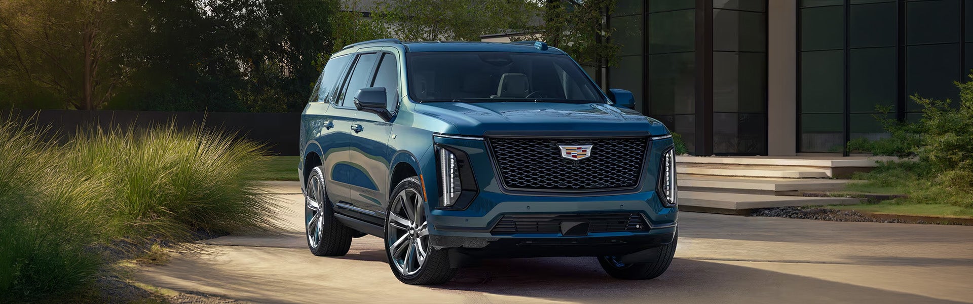 Blue Cadillac Escalade SUV parked in a paved driveway in front of a modern home.