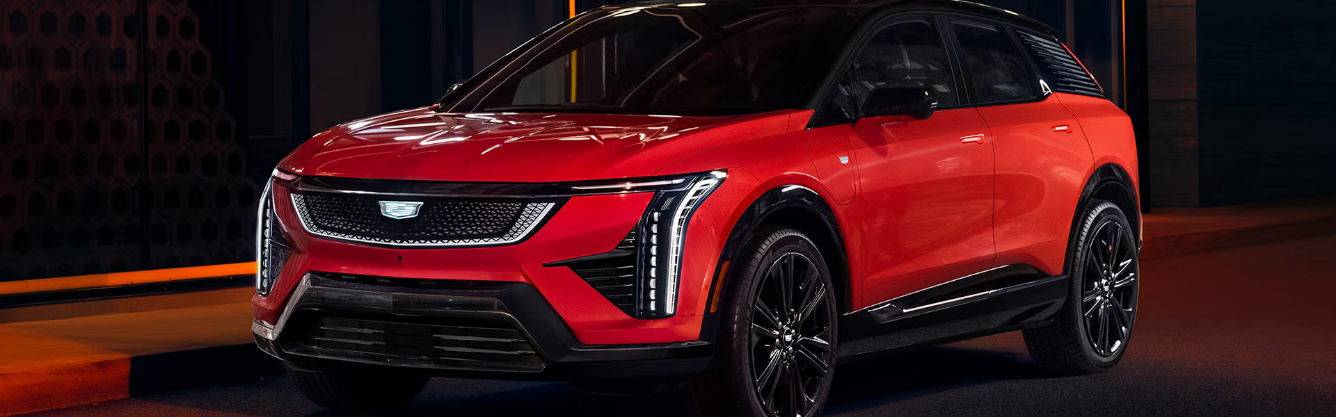 Red Cadillac Optiq electric SUV parked at night along an illuminated city street.